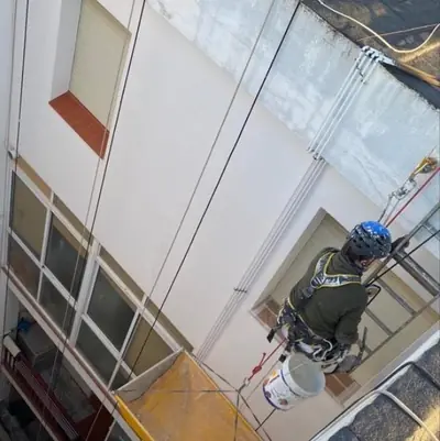 Operario colgado con cuerdas pintando la pared de un patio de luces